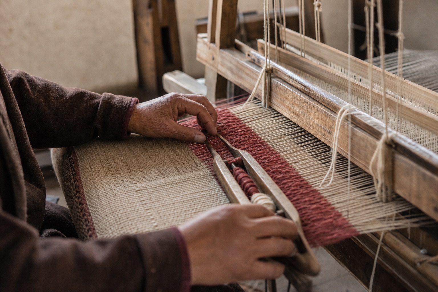 Hands guiding wool yarn across a wooden handloom