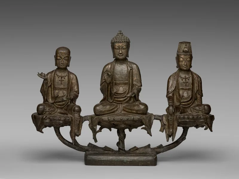 Bronze triad with Amitabha in the centre, shaved-headed Ksitigarbha on the viewer’s left and crowned Avalokiteshvara on the right, joined by a branching support.