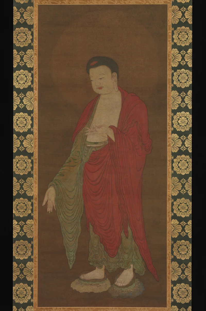 Chinese painting of a standing Amitabha Buddha in red and green robes, with one hand raised and the other extended down, within a patterned silk mounting.