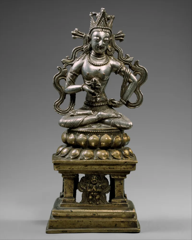 Crowned silver and bronze Amoghasiddhi with an emblem before his body, seated above a throne support and kneeling Garuda.