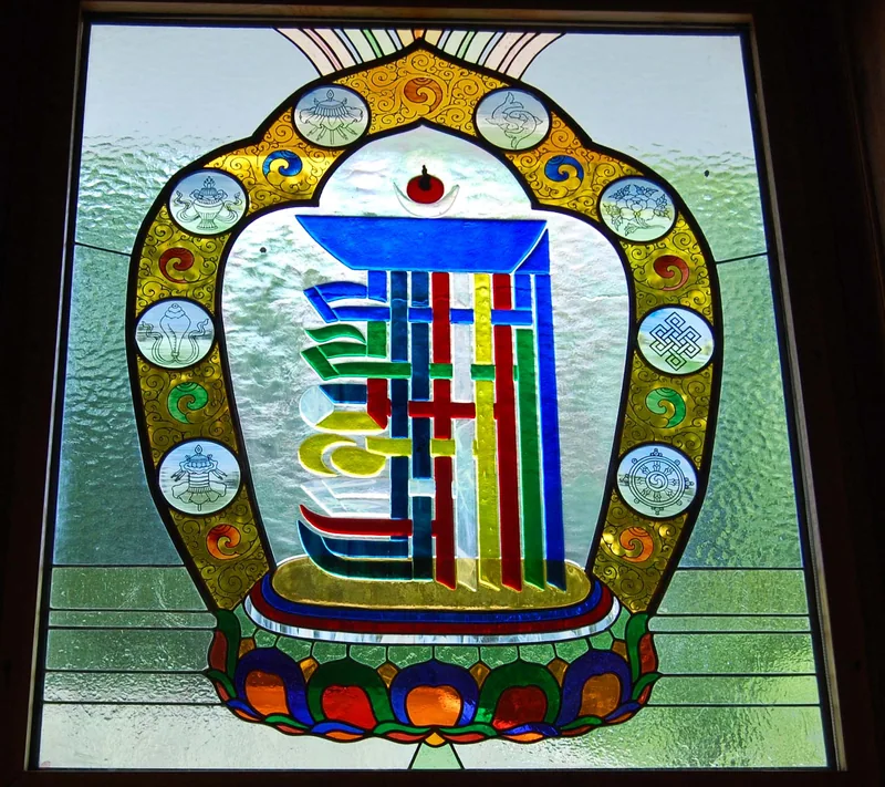 Stained-glass window with interwoven Kalachakra letterforms over a lotus and eight auspicious signs around the border.
