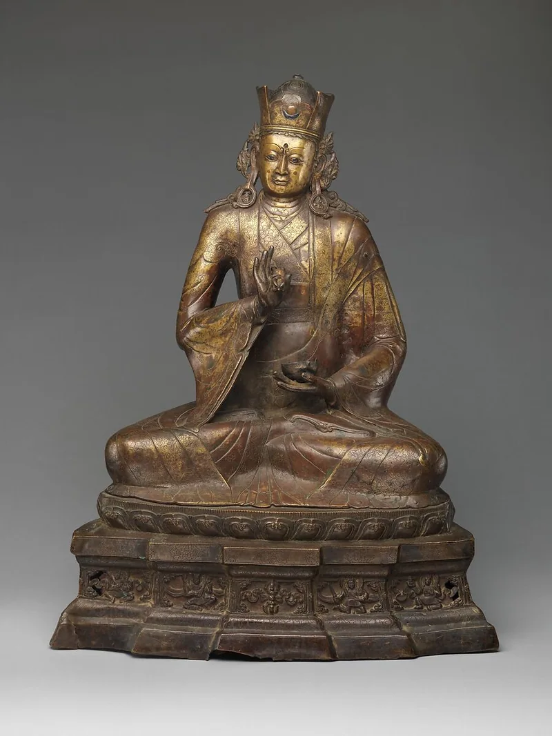 Copper-alloy Padmasambhava seated on a throne, holding an upright vajra and a cup low in his hands.