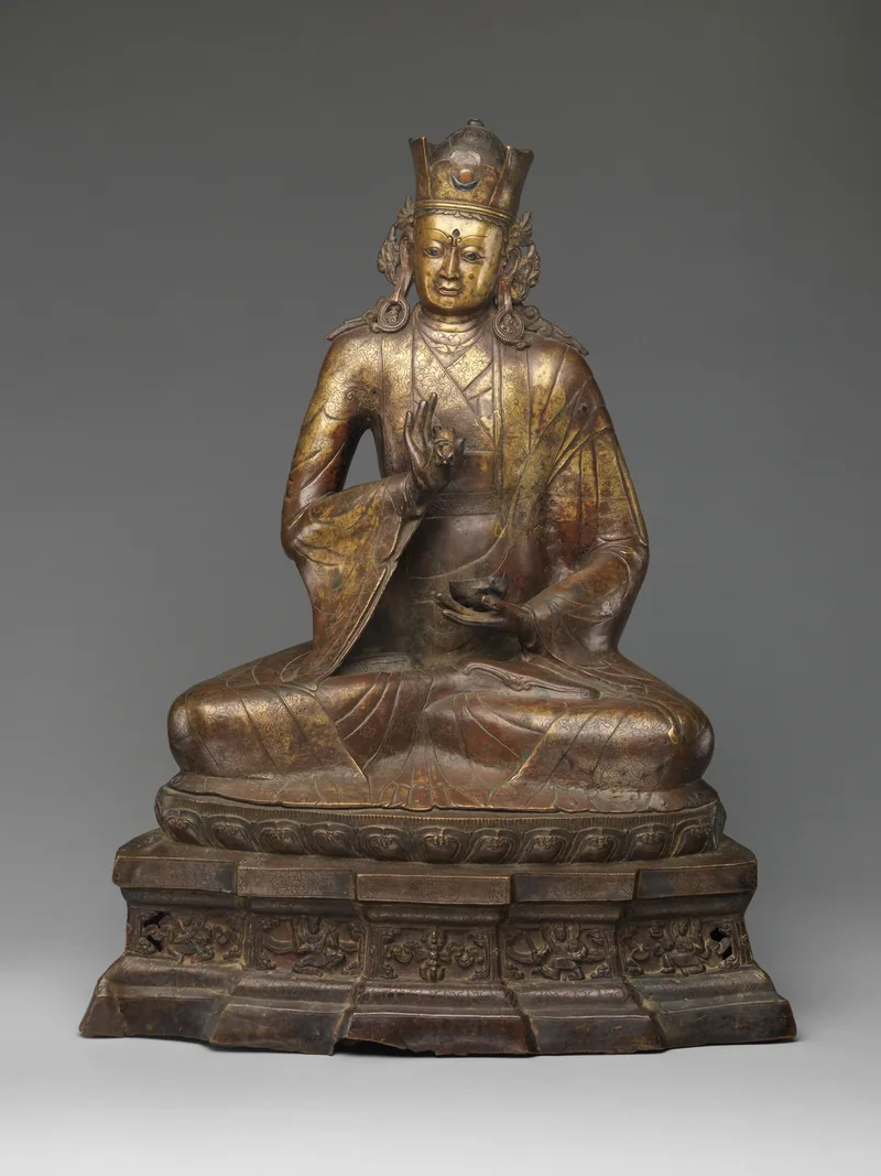 Seated Padmasambhava bronze wearing a cap and holding a vajra and skull cup, on an inscribed base.