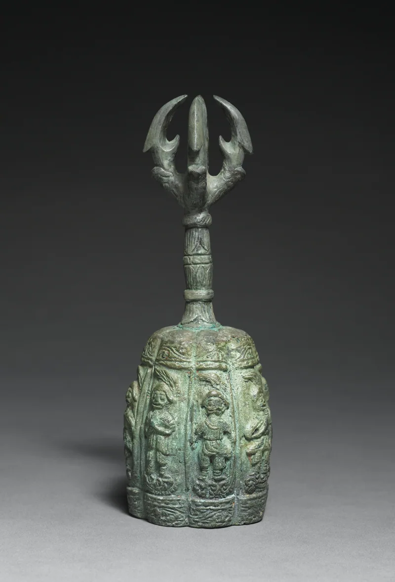 A green-patinated Korean bronze ritual bell with a vajra handle and figures on its body.