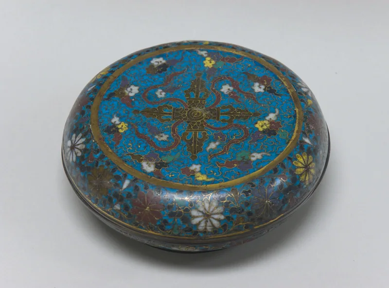 A blue Chinese cloisonné box with crossed vajras at the centre of its floral lid.