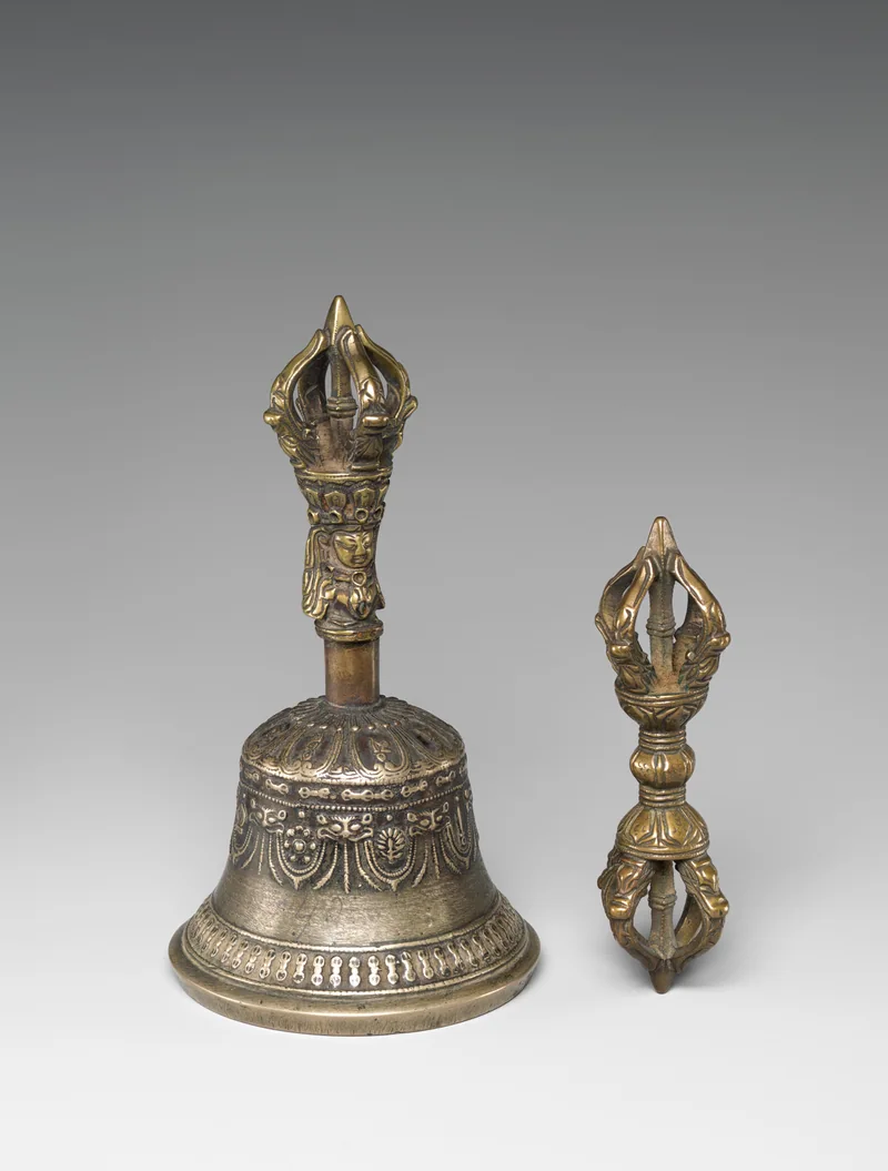 A Tibetan bronze ritual bell beside a dorje, with curved prongs and matching details.