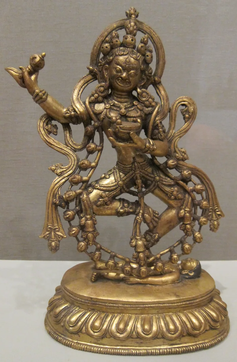 Gilded Vajrayogini sculpture with a raised curved knife, a cup and bent limbs, standing on a lotus pedestal.