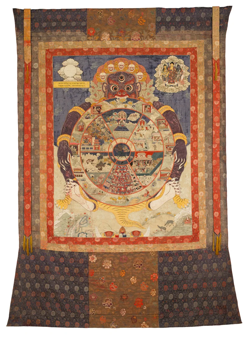 Mounted silk Wheel of Existence with central circular realms, a holding figure, two upper scenes and dark textile borders.