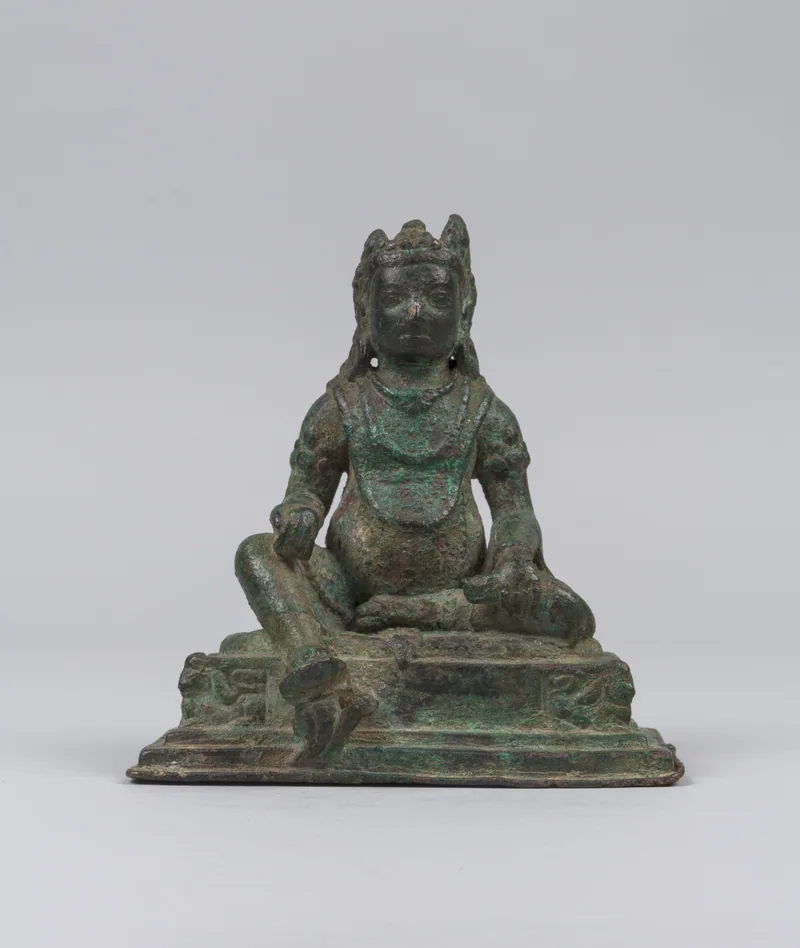 Seated Jambhala with a rounded torso, crown and extended leg in a Nepalese bronze